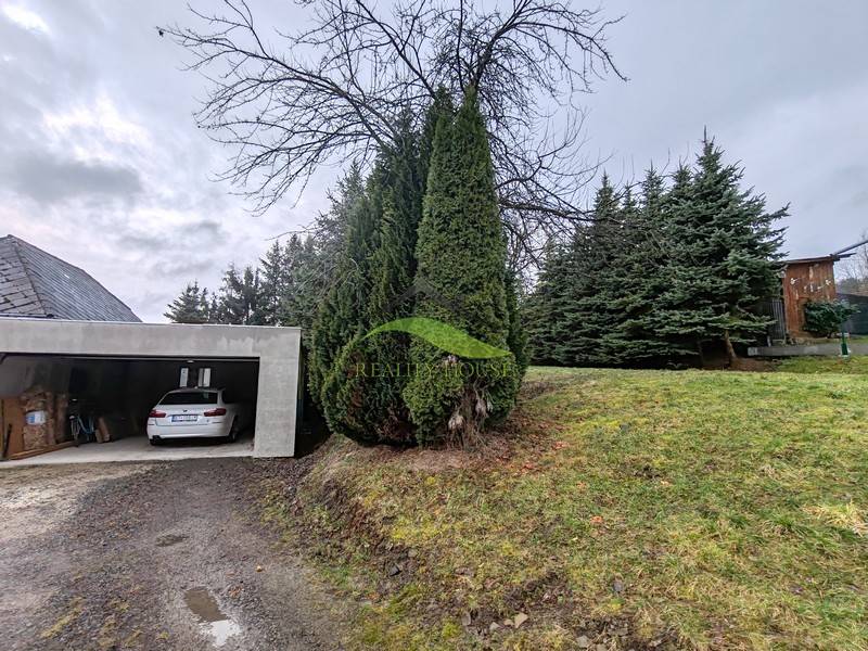 The garage at the family house on Hlavná Street in Piskorovce is surrounded by coniferous trees.
