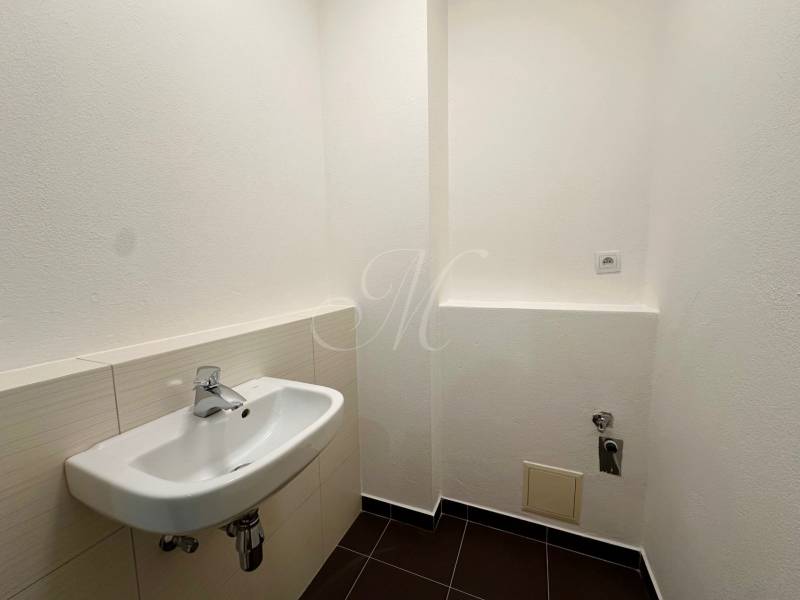 A toilet in a 4-room apartment with a white sink and black tiles.