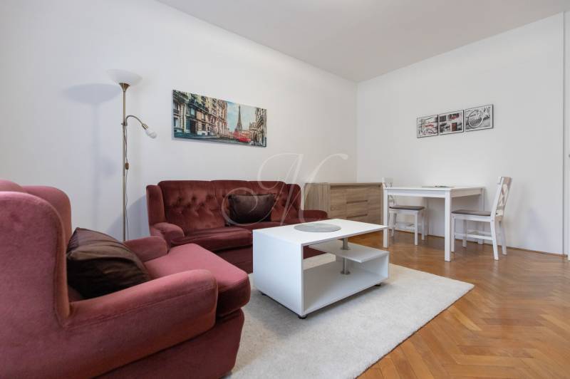 Living room of a two-room apartment with a burgundy sofa, white table on a floor with a wooden decor.