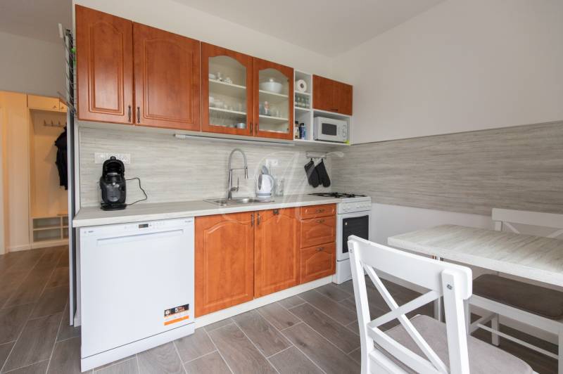 A kitchen in a 2-room apartment with wooden cabinets, a dishwasher, and a dining table.
