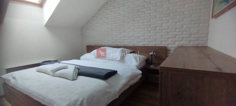A bedroom in a two-room apartment with a bed, a lamp, and a brick wall covering.