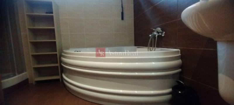 A bathroom with a corner bathtub, shower, and shelving cabinet in a 2-room apartment.