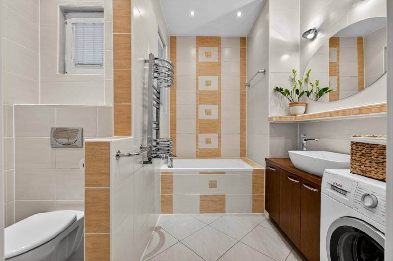 A bathroom with a bathtub, washing machine, sink, and decorative tiles in a 3-room apartment.