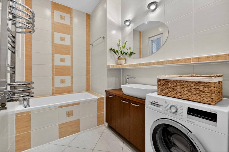 A bathroom in a 3-room apartment with a bathtub, washing machine, and brown tiles.