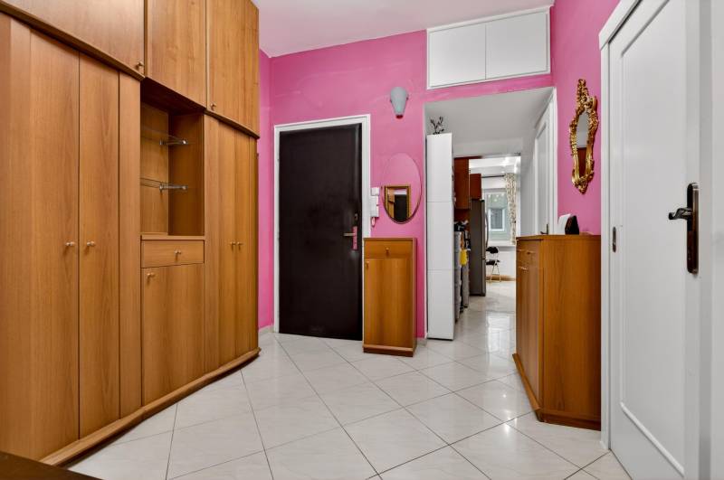 A spacious hallway of a 3-room apartment with wooden cabinets and pink walls.