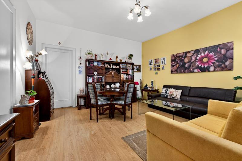Living room with wood-patterned flooring, paintings, a dark brown couch, and a dining table.