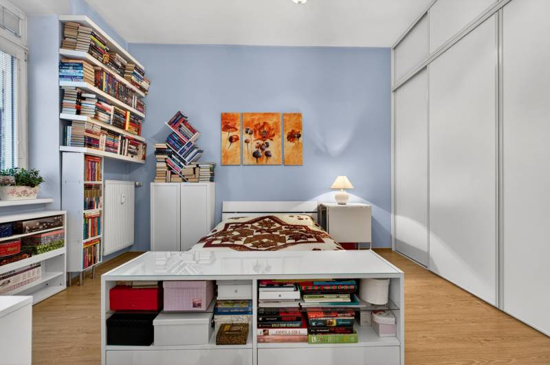 A bedroom with wood-patterned flooring, shelves full of books, and white furniture.