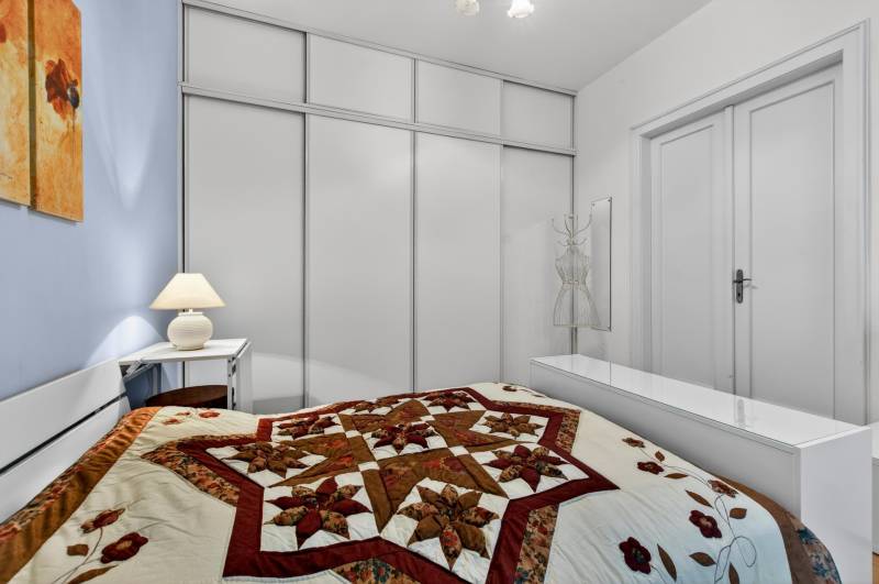 A bedroom with a decorative quilted bedspread in a 3-room apartment with minimalist furnishings.