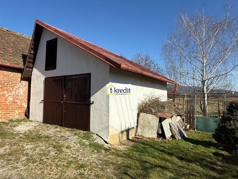 A cottage in Zlaté Moravce with wooden doors and a sloped roof in the yard.