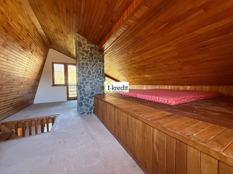 The attic of the cottage with wooden decor and a stone chimney resembles a cozy relaxation space.