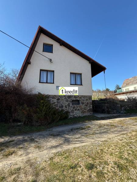 A cottage in Zlaté Moravce with a stone foundation and a sloped roof under a blue sky.