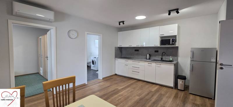 A kitchen with white cabinets and appliances in a 3-room apartment, with a wood-patterned floor.