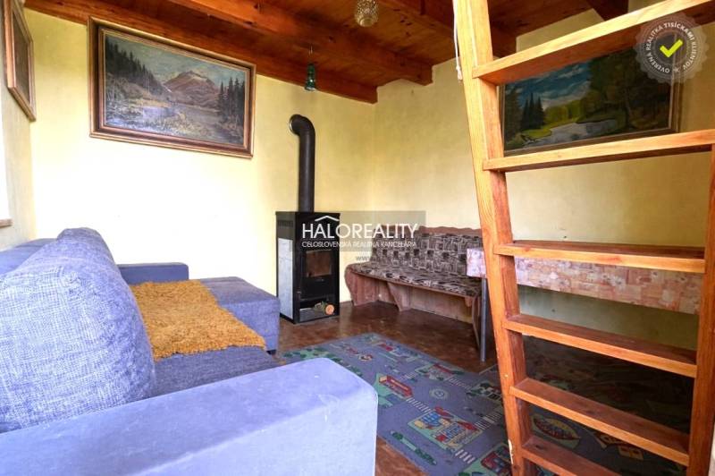 The interior of a cabin with a fireplace, wooden ceilings, and stairs to the attic.
