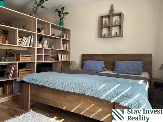 A bedroom in a one-room apartment with wooden furniture, a bed, and a shelving system.