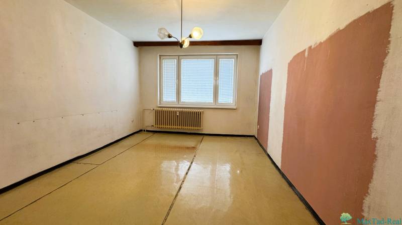 A room in a three-room apartment has a floor with a wood-effect decor and a radiator.