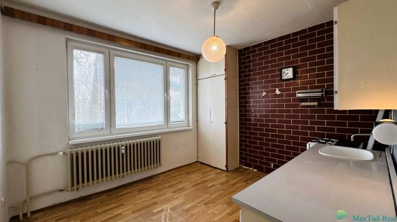 A kitchen with a wooden decor floor in a 3-room apartment with brown tiles.