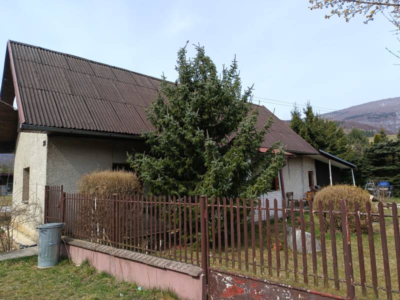 A family house in Vrícko with a fenced garden near a coniferous tree.