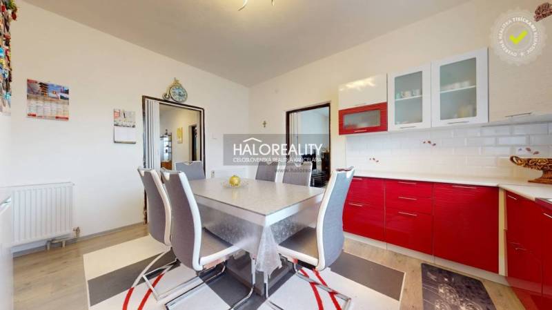 A dining room with a red kitchen unit and a wooden decor floor in a family house.