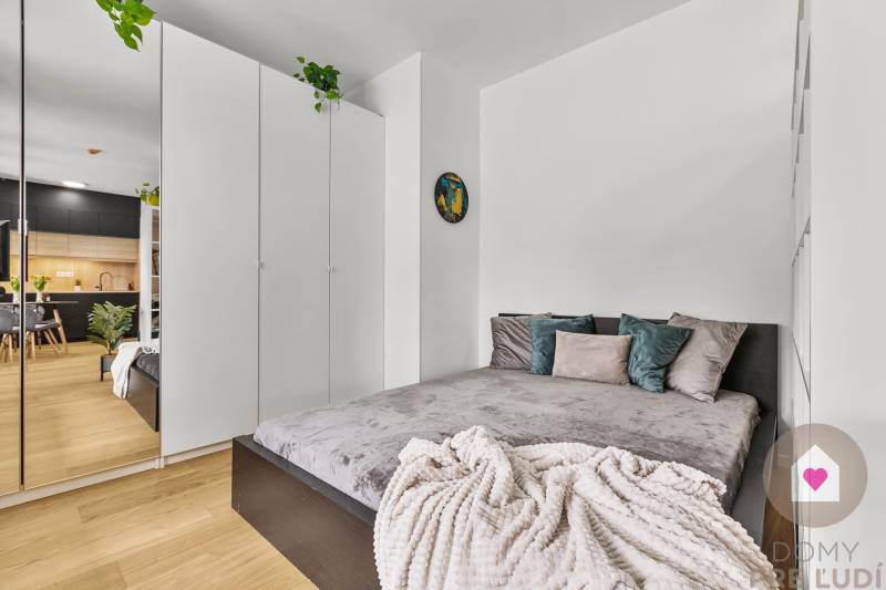 A bedroom in a studio apartment with a bed, a white wardrobe, and a wooden floor.