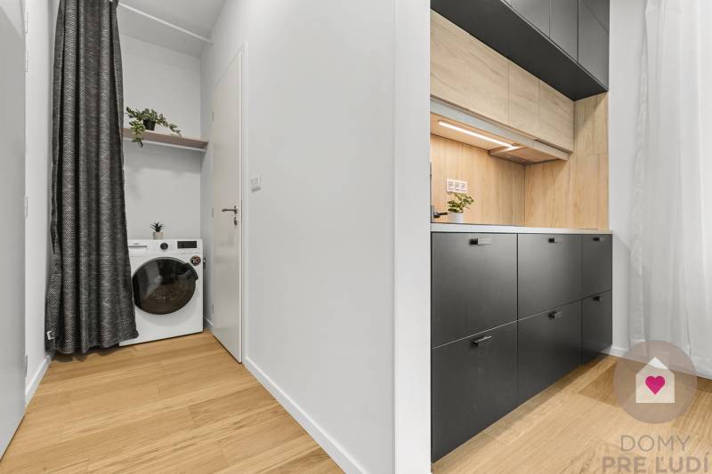 The kitchen in a studio apartment with a wood-patterned floor and a washing machine with a shelf.