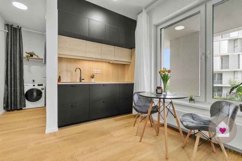 A kitchen in a studio apartment with black furniture, a washing machine, and a wooden decor floor.