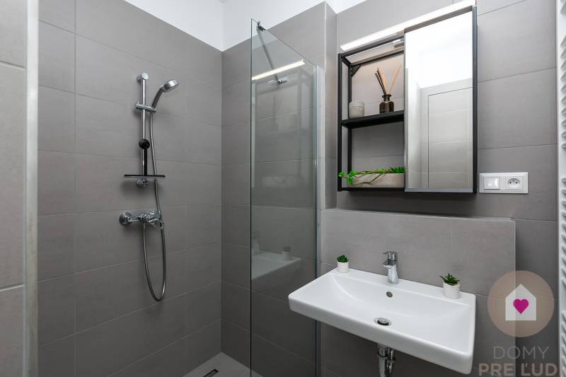 Gray bathroom with a shower, sink, and large mirror in a studio apartment.