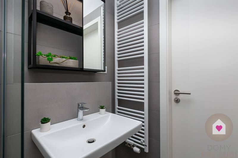 A bathroom in a studio apartment with a sink, ladder radiator, and storage shelves.