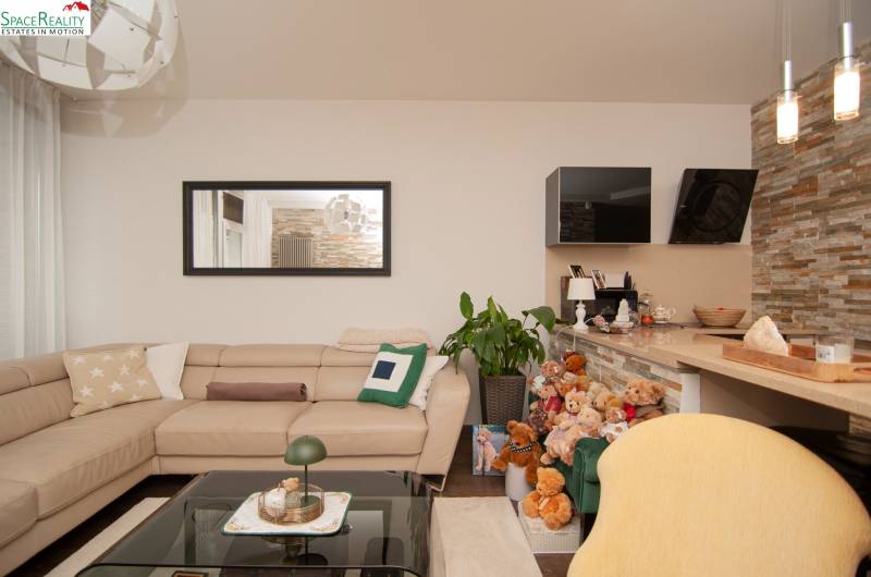 Living room in a two-room apartment with a beige leather sofa, a mirror, and plush teddy bears.