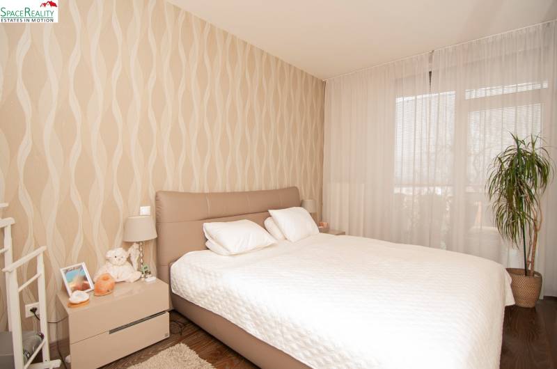 A bedroom in a two-room apartment with beige wallpaper and a wooden decor floor.