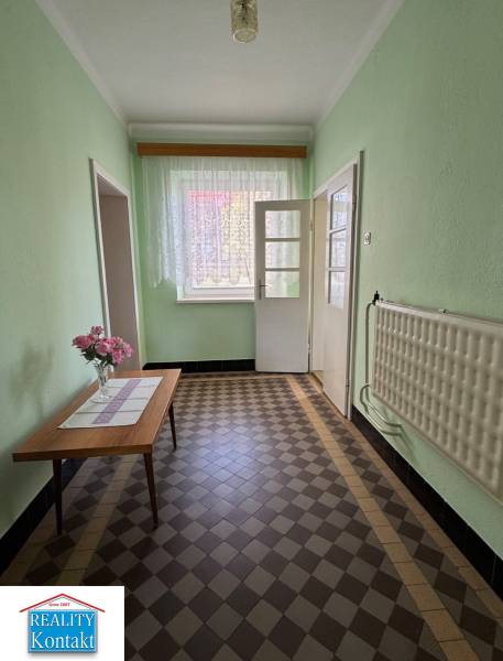 A hallway in a family house with flowers on the table and a tiled floor.