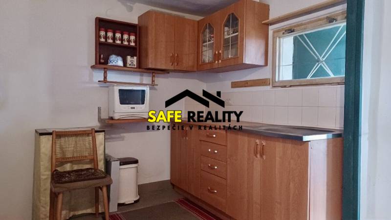 A kitchen in a cottage with wooden furniture and a microwave, floor with wooden decor.