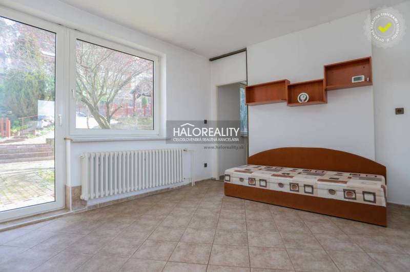 Interior of a family house with a bed, shelves, radiator, and a large window.