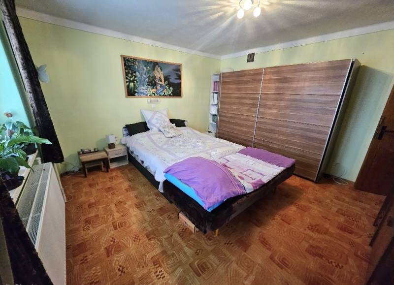 Bedroom in a family house with a bed, wardrobe, and wooden decor flooring.