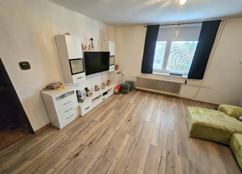 Living room in a family house with a television, white furniture, and a wooden decor floor.