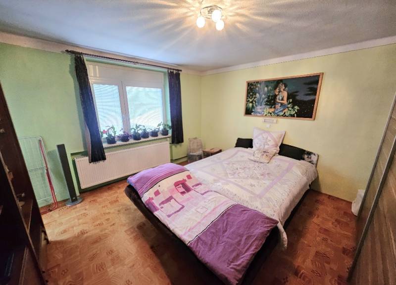 A bedroom in a family house with a bed, green walls, and a floor with a wooden decor.