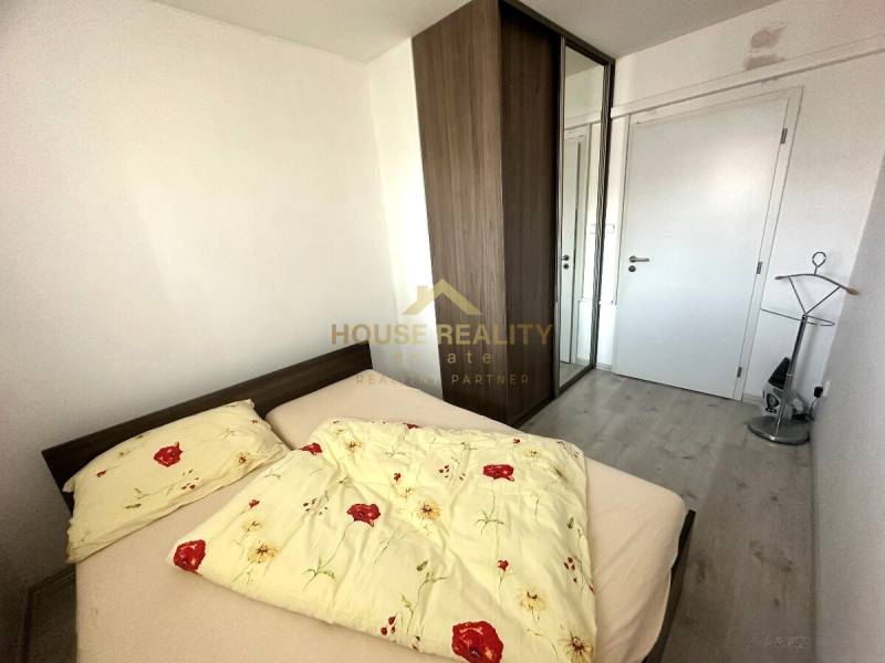 A bedroom in a 2-room apartment with a bed, built-in wardrobe, and wooden decor flooring.