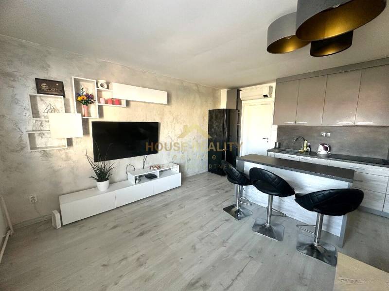 A kitchen in a 2-room apartment with a television, wood-patterned flooring, and a bar counter.