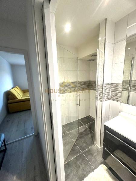 A bathroom in a 2-room apartment with a glass shower enclosure and large tiles.