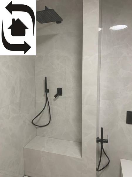 A shower corner in a 2-room apartment with a black faucet and a stone wall.