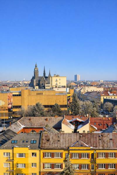 A view of the historical center of Košice, towers and buildings, with a blue sky in the background.