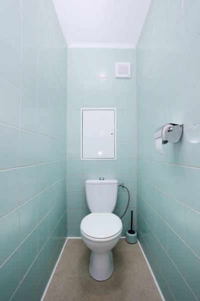 A toilet in a 3-room apartment with light blue tiles and a light-colored floor.