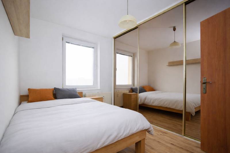 Bedroom in a 3-room apartment with wood-patterned flooring and a large mirrored wardrobe.