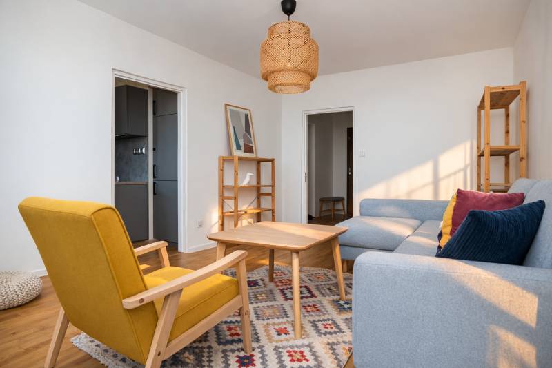 Living room in a 3-room apartment with wooden decor, a gray sofa, and a yellow armchair.