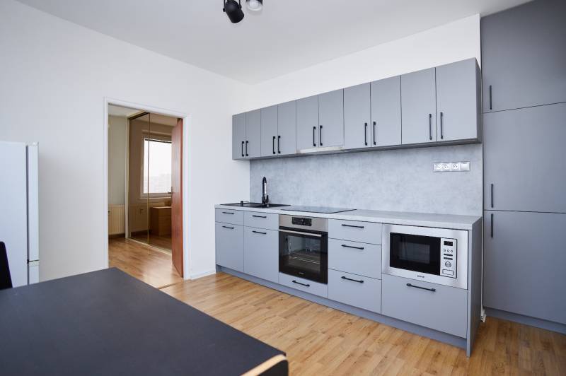 A kitchen in a 3-room apartment with modern appliances and a wooden decor floor.