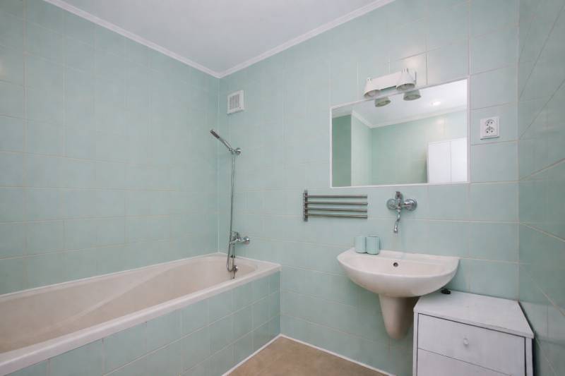 A bathroom in a 3-room apartment with a bathtub, a sink, a mirror, and light blue tiles.