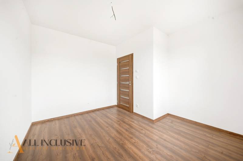 An empty room in a family house with white walls and a wood-patterned floor.