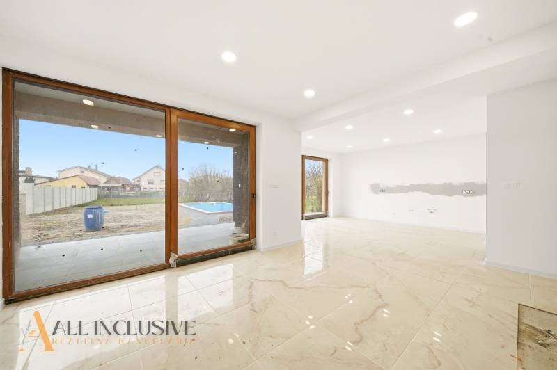 A spacious interior of a family house with large windows and a view of the garden with a swimming pool.