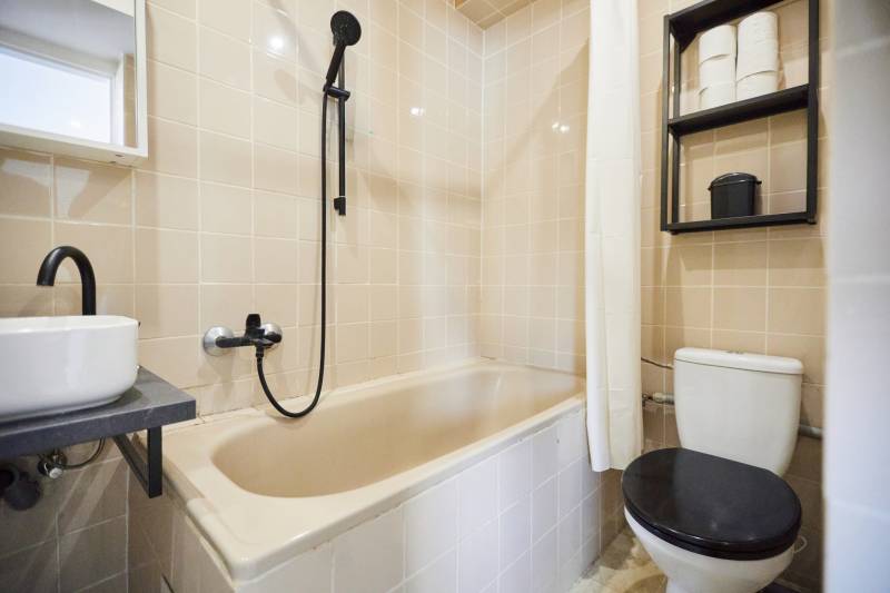 A bathroom with a bathtub, sink, shower, and toilet in a 2-room apartment.