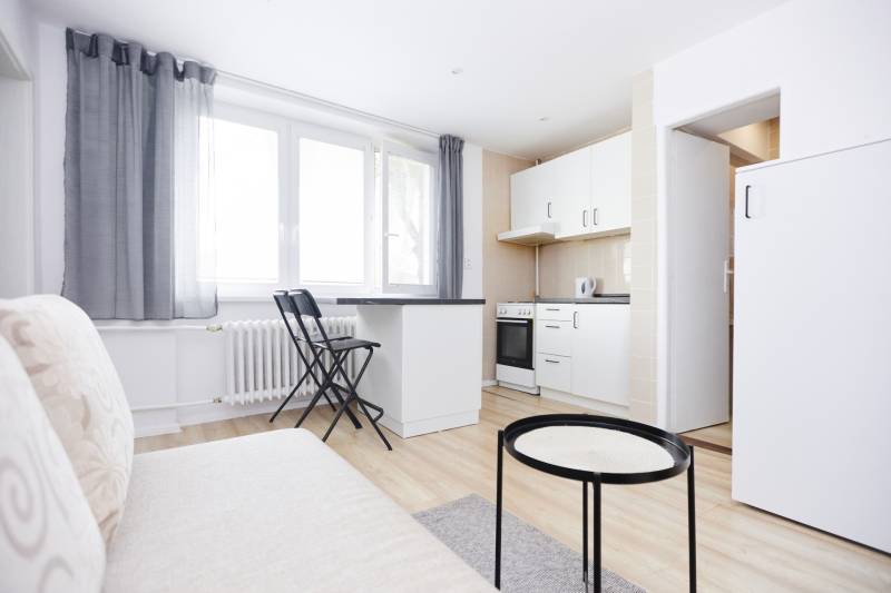 A kitchen in a 2-room apartment with white furniture and a wooden decor floor.