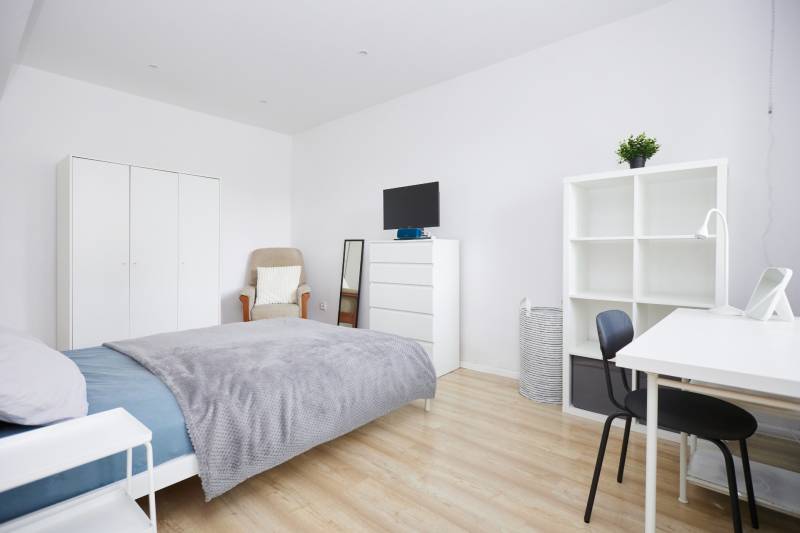 Bedroom in a 2-room apartment with white furniture and a wood-patterned floor.